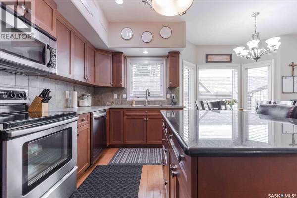 Kitchen with dark wood cabinets, stainless steel appliances, and granite countertops. - 107 Galloway Road, Saskatoon