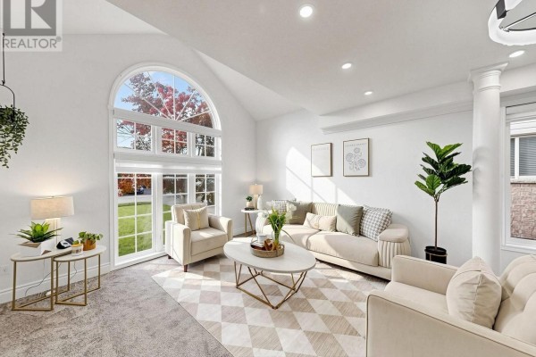 Living room with a vaulted ceiling, large arched window, beige sofa and armchairs, and a patterned rug. - 107 Green Bank Drive, Cambridge