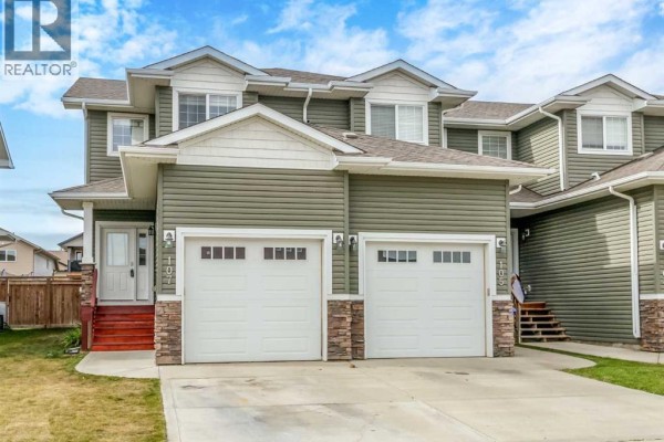 Front exterior of the townhouse complex at 107 Henderson Crescent, showing two attached units with garage doors. - 107 Henderson Crescent, Penhold