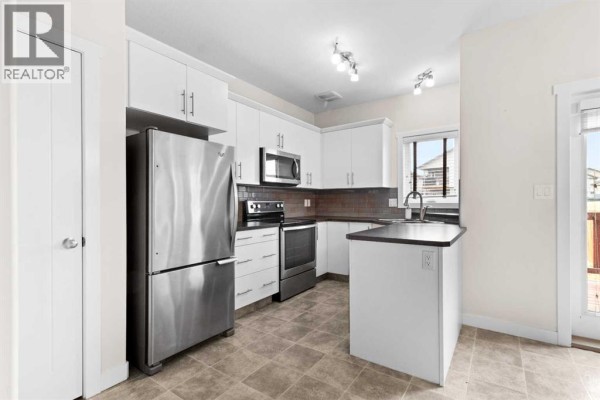 Kitchen with stainless steel appliances, white cabinets, dark countertops, and tiled backsplash, with a view of the backyard. - 107 Henderson Crescent, Penhold