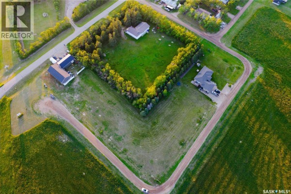Aerial view of houses and treed areas surrounding a large grassy lot. - 107 Keating Court, Estevan Rm No  5