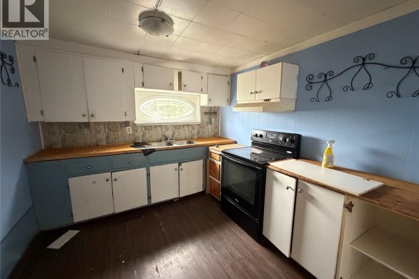 A kitchen with blue walls, white cabinets, a black stove, and wood countertops. - 107 Main Street, Shell Lake