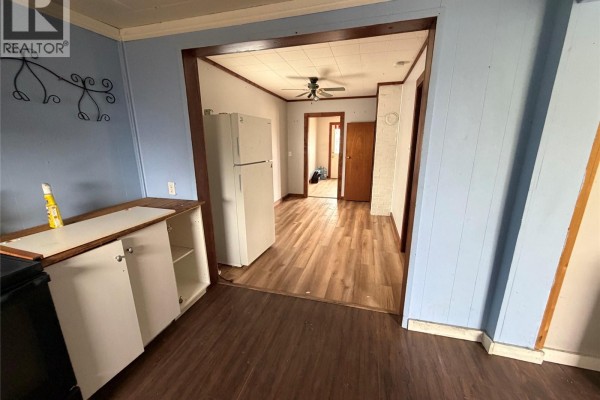 View from the kitchen into a dining area with a white refrigerator and wood floors. - 107 Main Street, Shell Lake