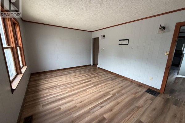 A living room with light gray walls, wood trim, and wood laminate flooring. - 107 Main Street, Shell Lake