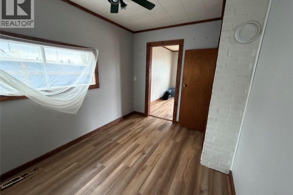 A small bedroom with light gray walls, wood trim, and a window covered by plastic. - 107 Main Street, Shell Lake