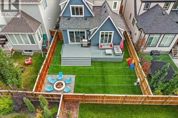 Aerial view of a fenced backyard with artificial turf, a deck, and a fire pit. - 107 Masters Way Se, Calgary