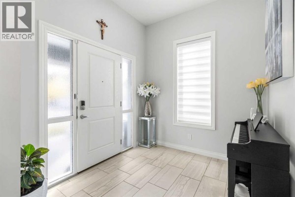 Interior view of a bright foyer with a white door, tile floor, and a digital piano. - 107 Masters Way Se, Calgary