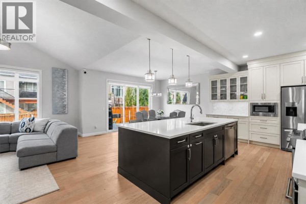 Open-concept kitchen and living area with a large island, grey sectional sofa, and dining table. - 107 Masters Way Se, Calgary