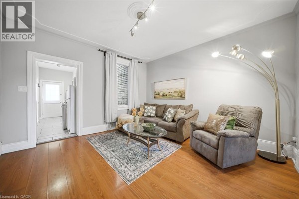 Living room with hardwood floors, sofa, armchair, rug, and floor lamp. - 107 Queen Street S Unit# 1, Hamilton