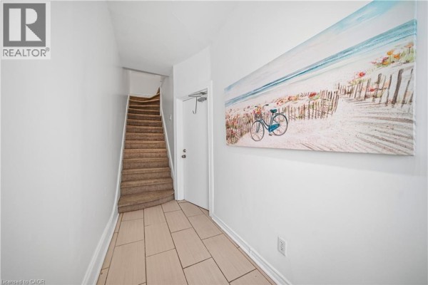 Hallway with tiled floor, staircase, and a colorful beach-themed painting on the wall. - 107 Queen Street S Unit# 2, Hamilton