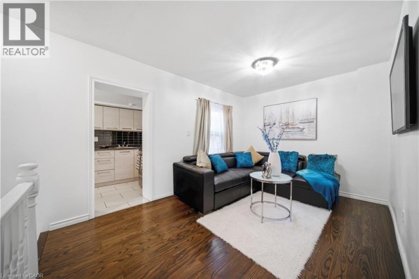 Living room with dark wood floors, black leather sofa, white rug, and entrance to kitchen. - 107 Queen Street S Unit# 2, Hamilton