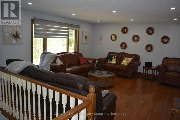 Living room with multiple brown leather sofas, hardwood floors, large window, and recessed lighting. - 107 South Baptiste Lake Road, Hastings Highlands