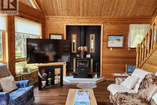 Living room with wood paneling, a wood-burning stove, and a large television. - 107 Spruce Crescent, Brightsand Lake