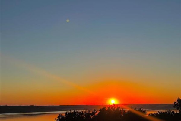 Vibrant orange sunset over a wide, calm lake with silhouetted trees against a gradient sky. - 107 Sunset Drive, Lake Of The Prairies
