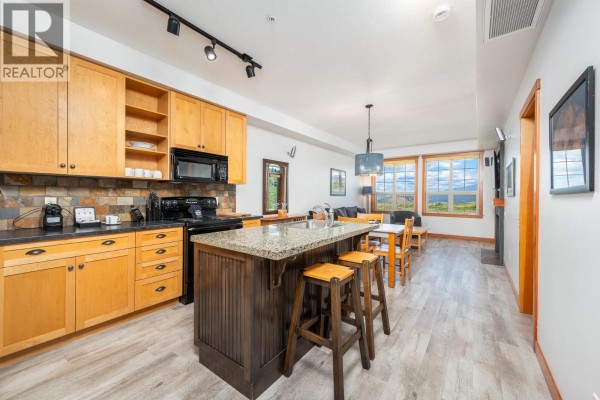Close-up of a black electric stove, microwave, and wood cabinets in a kitchen with a stone tile backsplash. - 107 Village Centre Court Unit# 214, Vernon