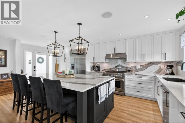 Spacious kitchen with white cabinets, quartz countertops, stainless steel appliances, and a center island. - 1070 Maccleave Avenue, Penticton