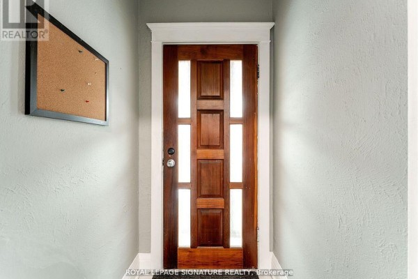 Interior view of a wooden front door with glass panels and a cork bulletin board on the wall. - 1070 Shaw Street, Toronto