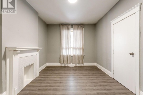 Bedroom with a white fireplace surround, grey walls, sheer curtains, and grey wood-look flooring. - 1070 Shaw Street, Toronto