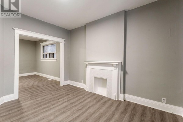 Living room with a white fireplace surround, grey walls, and an opening to another room. - 1070 Shaw Street, Toronto
