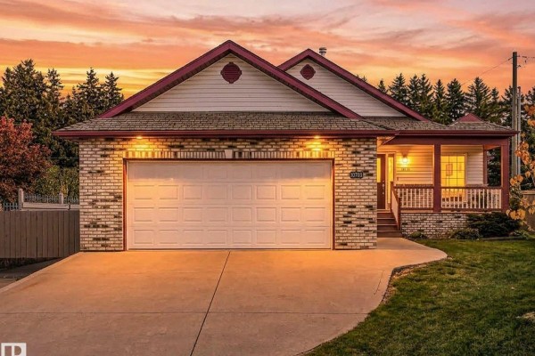 Front view of the house at dusk, with brick exterior, white garage door, and warm lighting. - 10703 6 Av Sw, Edmonton
