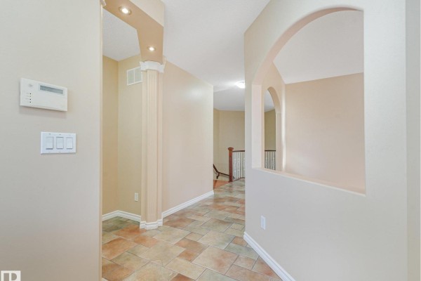 Interior hallway with beige walls, tiled floor, and an arched opening revealing a staircase. - 10703 6 Av Sw, Edmonton