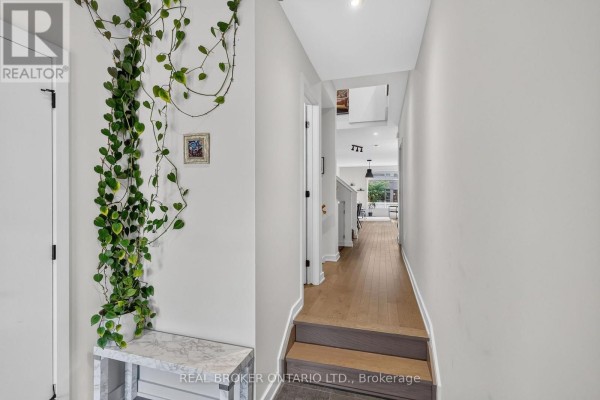 Interior hallway with light grey walls, wood flooring, a staircase, and a large hanging plant. - 1071 Lunar Glow Crescent, Ottawa