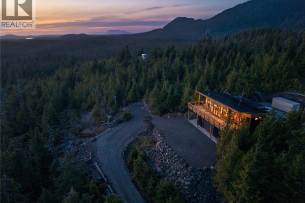 Nighttime aerial view of a illuminated modern house on a forested hillside with ocean backdrop. - 1071 Uplands Close, Ucluelet