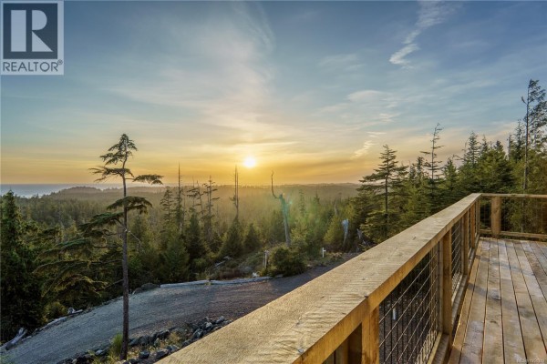 Wooden deck and railing facing a vast forest and ocean landscape at sunset. - 1071 Uplands Close, Ucluelet