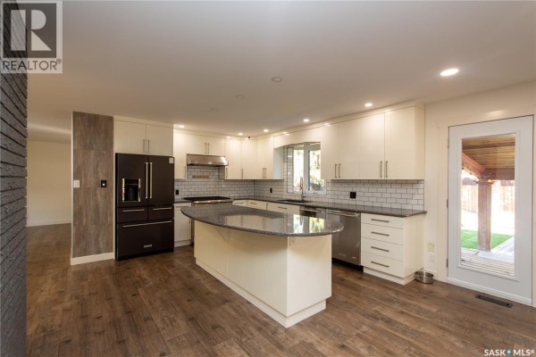 Modern kitchen with white cabinets, stainless steel appliances, and an island with a granite countertop. - 10710 Meighen Crescent, North Battleford
