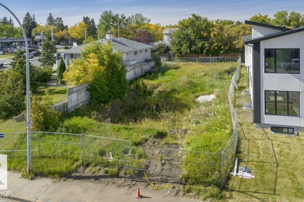 View of the undeveloped land from street level, surrounded by temporary fencing and adjacent modern townhouses. - 10712 149 St Nw, Edmonton