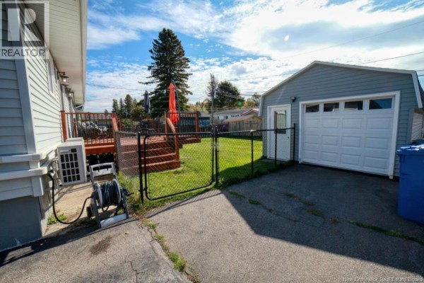 Backyard view showing a wooden deck, chain link fence, and detached garage. - 1073 Rockland Drive, Bathurst