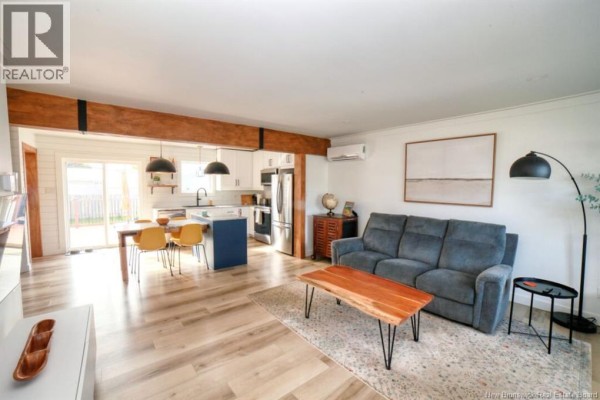 Living room with grey sofa and coffee table, open to dining area and kitchen. - 1073 Rockland Drive, Bathurst
