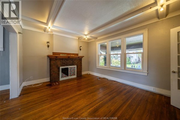 Living room showing a brick fireplace, hardwood floors, and large windows with a view of houses outside. - 1076 Dougall Avenue Unit# Main, Windsor