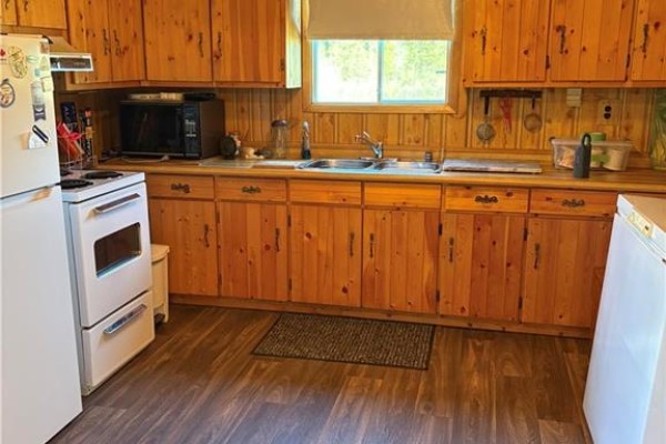 Kitchen with light wood cabinets, white appliances, double sink, and wood paneling on walls. - 1076 Howard Rd, Howard