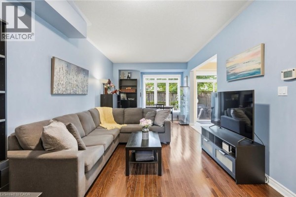 Living room with grey sectional sofa, dark wood floors, and large window view. - 1076 Ryckman Common, Burlington