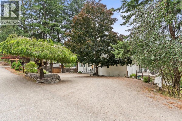 Gravel driveway leading to the side and back of a white house with trees. - 10771 Pinecrest Road, Vernon