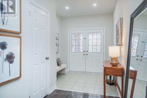 Interior hallway showing double front doors, tiled floor, and a wooden console table. - 1079 Job Crescent, Milton
