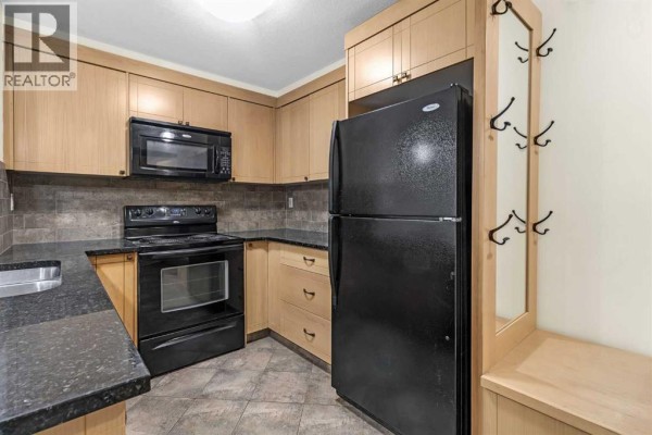 U-shaped kitchen with light wood cabinets, black appliances, and granite countertops. - 108, 315 50 Avenue Sw, Calgary