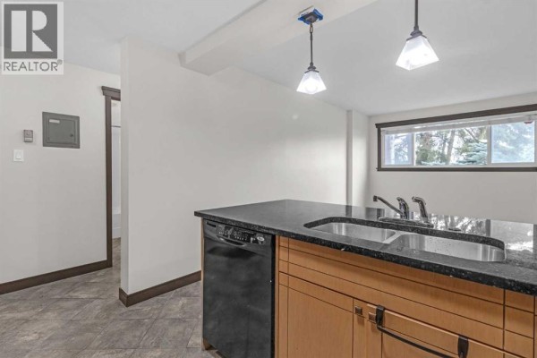 Kitchen island with granite countertop and two bar stools, adjacent to the entrance. - 108, 315 50 Avenue Sw, Calgary