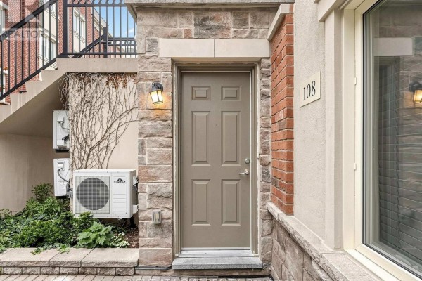 Front door of a townhouse with brick and stone exterior and air conditioning units. - 108 - 17 Coneflower Crescent, Toronto