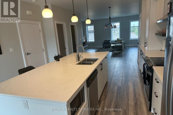 Open-concept kitchen and living area with island, sofa, and large windows. - 108 - 361 Quarter Town Line, Tillsonburg
