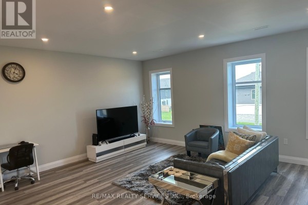 Living room with gray sofa, armchair, television, desk, and wood-look flooring. - 108 - 361 Quarter Town Line, Tillsonburg