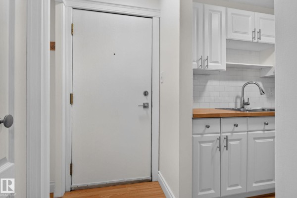 Apartment entryway with a white door and a small white kitchen with light wood countertops. - #108 10520 80 Av Nw, Edmonton