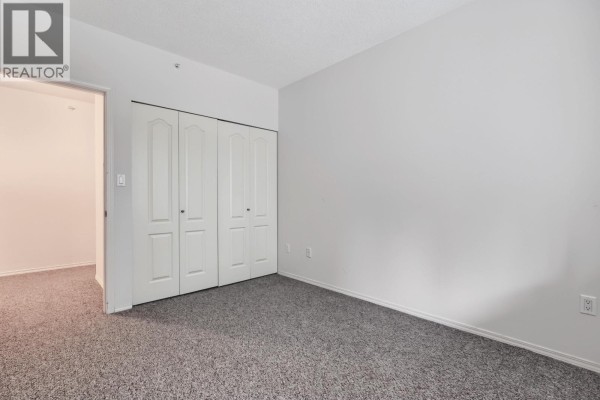 Bedroom with grey carpet, white bi-fold closet doors, and doorway to hall. - 108 12148 224 Street, Maple Ridge