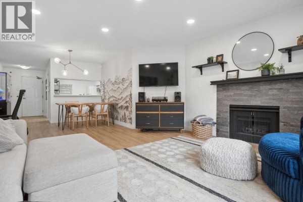 Living room and dining area with fireplace, sectional sofa, dining table with chairs, and mountain-themed wallpaper. - 108 1655 Augusta Avenue, Burnaby
