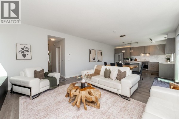 Open concept living and dining area with white sofas, a large wood dining table, and a modern kitchen. - 108 3500 Burke Village Promenade, Coquitlam