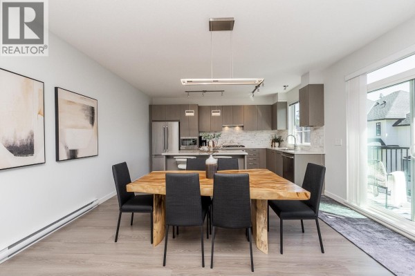 Dining area with a wooden table and chairs, adjacent to a modern kitchen with grey cabinetry and stainless steel appliances. - 108 3500 Burke Village Promenade, Coquitlam
