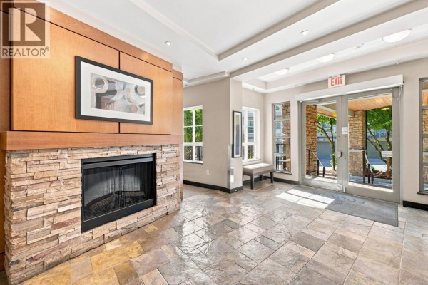 Building lobby with a stone fireplace, tiled flooring, seating area, and glass doors leading outside. - 108 9233 Government Street, Burnaby