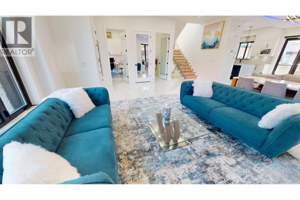 Spacious living room with teal sofas, fireplace, and view of stairs and dining area. - 108 E 51st Avenue, Vancouver
