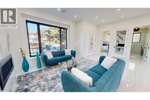 Living room with large window, teal sofas, coffee table, and view of hallway and fireplace. - 108 E 51st Avenue, Vancouver
